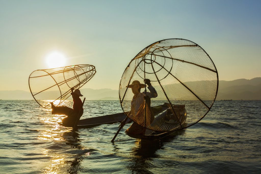 Myanmar travel attraction landmark - two traditional Burmese fishermen at Inle lake, Myanmar famous for their distinctive one legged rowing style on sunrise sunset
